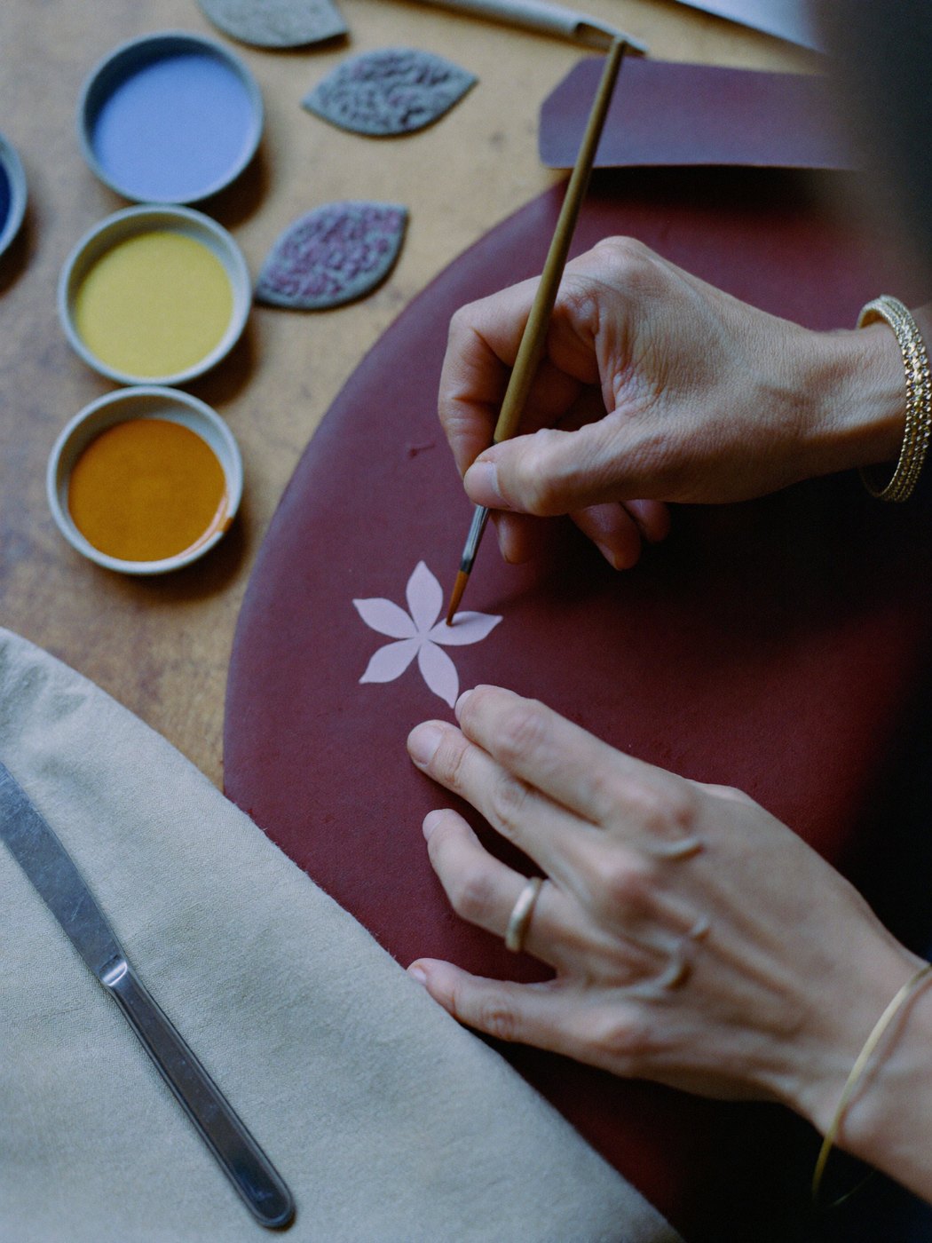 Hand-painting a Persian flower motif onto burgundy leather at the bench